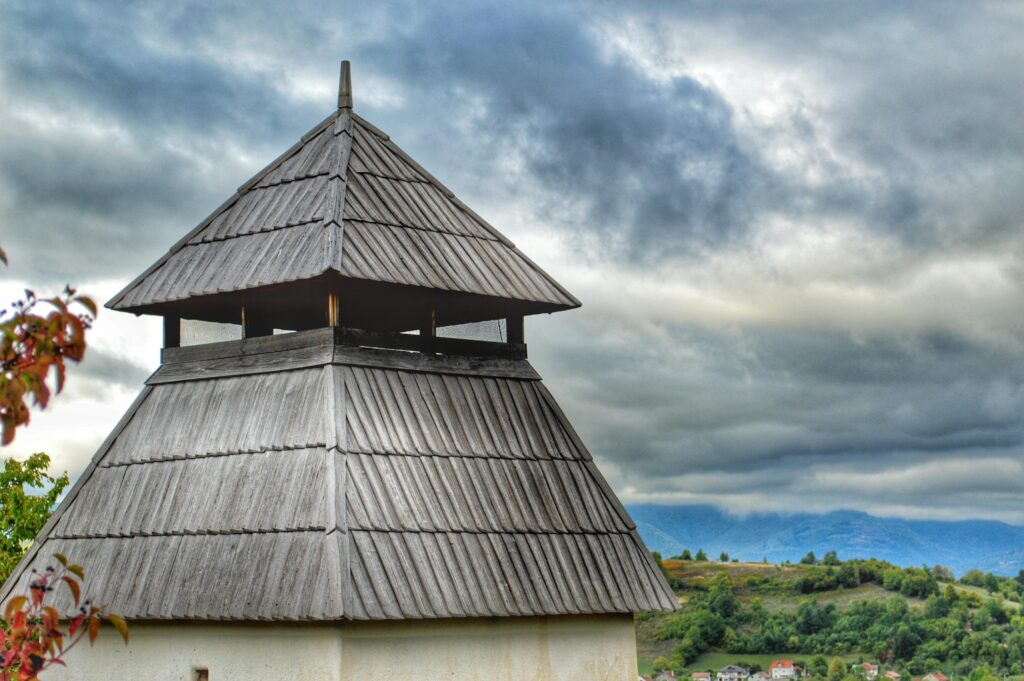 A wooden tower stands against a dramatic cloudy sky with mountain views.