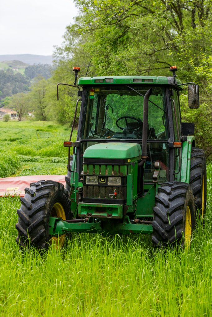 A green tractor parked in a lush, green field surrounded by trees.